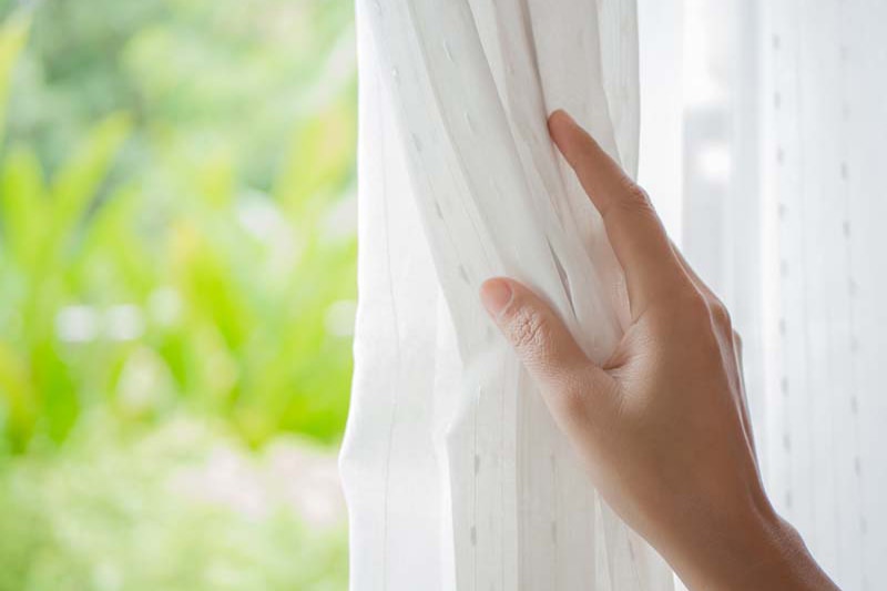 womans hand opening white linen curtain