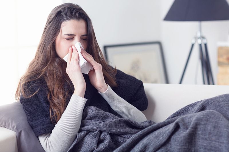 What Does Indoor Air Quality Have to Do With Allergies? Image of woman sitting on couch and blowing her nose.